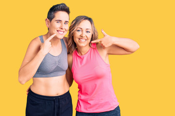 Fototapeta na wymiar Couple of women wearing sportswear smiling cheerful showing and pointing with fingers teeth and mouth. dental health concept.