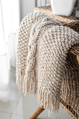 Detail of hand-woven beige wool blanket on wicker chair.