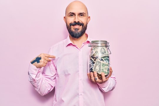 Young handsome man holding jar with savings pointing finger to one self smiling happy and proud