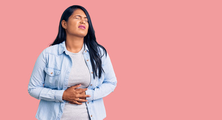 Hispanic woman with long hair wearing casual denim jacket with hand on stomach because indigestion, painful illness feeling unwell. ache concept.