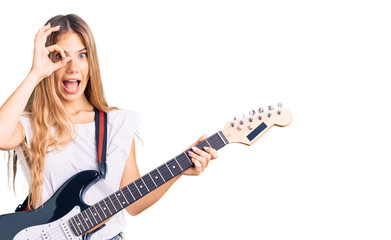 Fototapeta premium Beautiful caucasian woman with blonde hair playing electric guitar smiling happy doing ok sign with hand on eye looking through fingers