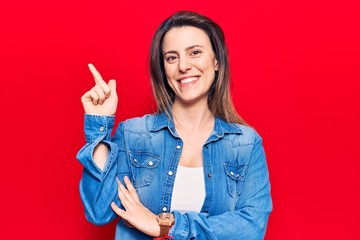 Young beautiful woman wearing casual clothes with a big smile on face, pointing with hand and finger to the side looking at the camera.