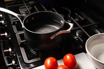 Black pot with water boiling on black stove with white bowl and red tomatoes