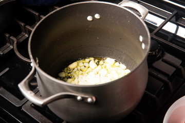 Black pot on stove with oil, onions and garlic preparing a meal