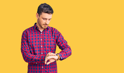 Handsome young man with bear wearing casual shirt checking the time on wrist watch, relaxed and...