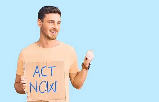 Handsome young man with bear holding act now banner pointing thumb up to the side smiling happy with open mouth