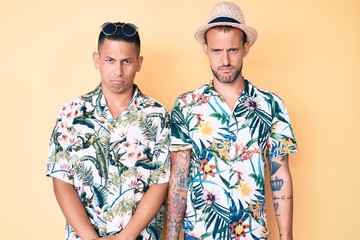 Young gay couple of two men wearing summer hat and hawaiian shirt depressed and worry for distress, crying angry and afraid. sad expression.