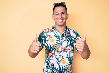 Young handsome latin man wearing summer clothes success sign doing positive gesture with hand, thumbs up smiling and happy. cheerful expression and winner gesture.