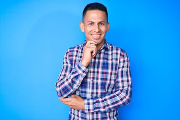 Young handsome latin man wearing casual clothes looking confident at the camera with smile with crossed arms and hand raised on chin. thinking positive.