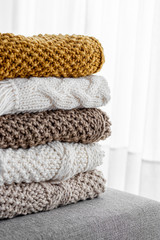 Detail of a stack of five woolen blankets of various colors beige, brown, white, hand-woven on a gray armchair.