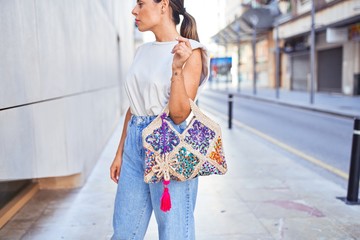 Fototapeta premium Young woman wearing fasionable clothes holding colorful and trendy bag at the city