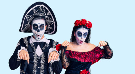 Young couple wearing mexican day of the dead costume over background pointing down with fingers showing advertisement, surprised face and open mouth