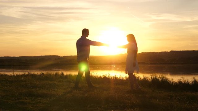 Young free couple dancing at sunset on beach. Happy guy and girl waltz in evening in a summer park. Enamored man and woman dance in the bright rays of the sun on background of the lake.