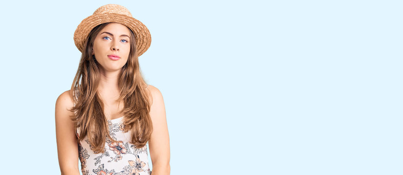 Beautiful caucasian young woman wearing summer hat relaxed with serious expression on face. simple and natural looking at the camera.