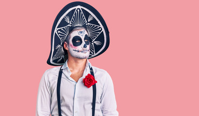 Man wearing day of the dead costume over background smiling looking to the side and staring away thinking.