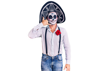Man wearing day of the dead costume over background smiling doing phone gesture with hand and fingers like talking on the telephone. communicating concepts.