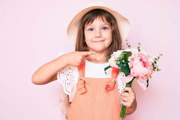 Little caucasian kid girl with long hair holding flower wearing spring hat smiling happy pointing with hand and finger