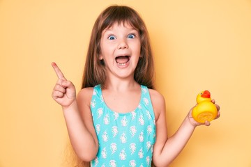 Little caucasian kid girl with long hair wearing swimsuit and holding duck toy smiling with an idea...