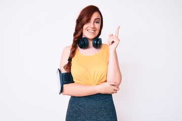 Young beautiful woman wearing gym clothes and using headphones smiling happy pointing with hand and finger to the side