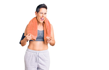 Young woman with short hair wearing sportswear and towel using smartphone pointing fingers to camera with happy and funny face. good energy and vibes.