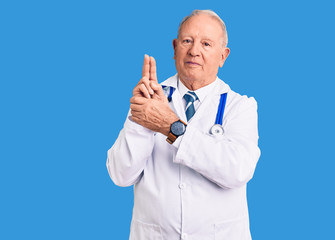 Senior handsome grey-haired man wearing doctor coat and stethoscope holding symbolic gun with hand gesture, playing killing shooting weapons, angry face