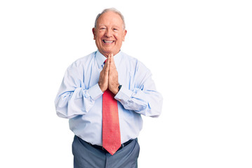 Senior handsome grey-haired man wearing elegant tie and shirt praying with hands together asking...