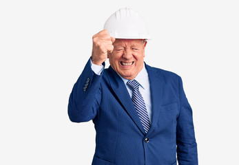 Senior handsome grey-haired man wearing suit and architect hardhat angry and mad raising fist frustrated and furious while shouting with anger. rage and aggressive concept.