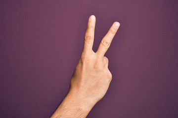 Hand of caucasian young man showing fingers over isolated purple background counting number 2 showing two fingers, gesturing victory and winner symbol