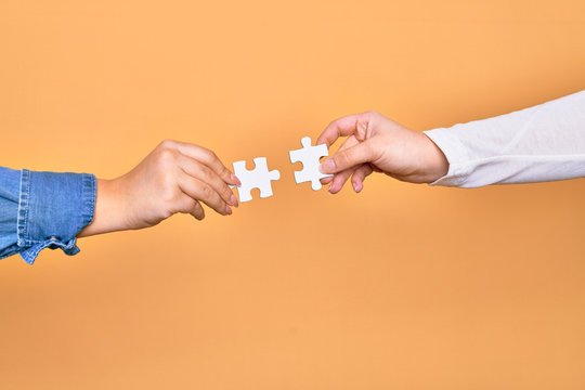 Hands of caucasian young people connecting pieces of puzzle over isolated yellow background