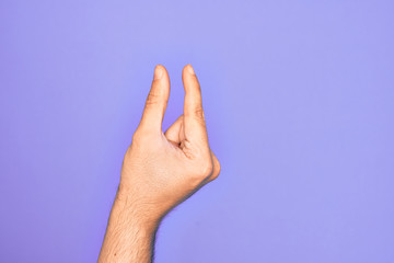 Hand of caucasian young man showing fingers over isolated purple background picking and taking invisible thing, holding object with fingers showing space