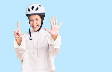 Beautiful brunette young woman wearing bike helmet and sporty clothes showing and pointing up with fingers number six while smiling confident and happy.