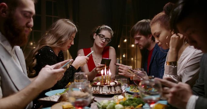 Group of bored multiethnic friends at a birthday party. Unhappy people staring at their phones scrolling through social media - real people concept 4k footage