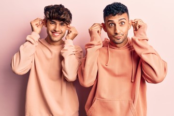 Young gay couple wearing casual clothes smiling pulling ears with fingers, funny gesture. audition...