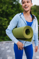 Young woman walking in urban park holding fitness rug.