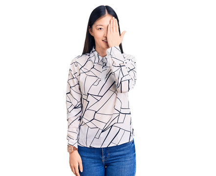Young beautiful chinese woman wearing casual shirt covering one eye with hand, confident smile on face and surprise emotion.
