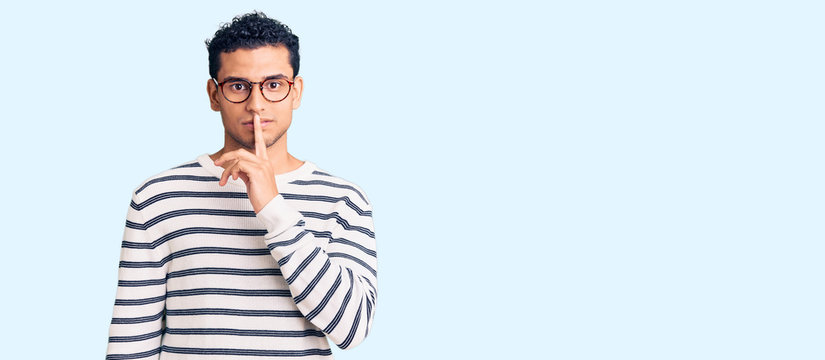 Hispanic handsome young man wearing casual clothes and glasses asking to be quiet with finger on lips. silence and secret concept.
