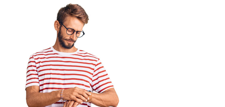 Handsome blond man with beard wearing casual clothes and glasses checking the time on wrist watch, relaxed and confident