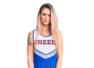 Young beautiful blonde woman wearing cheerleader uniform skeptic and nervous, frowning upset...