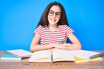 Cute hispanic child girl studying for school exam sitting on the table with a happy and cool smile on face. lucky person.