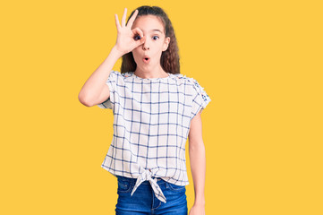 Fototapeta premium Cute hispanic child girl wearing casual clothes doing ok gesture shocked with surprised face, eye looking through fingers. unbelieving expression.