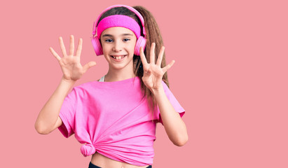 Obraz na płótnie Canvas Cute hispanic child girl wearing gym clothes and using headphones showing and pointing up with fingers number nine while smiling confident and happy.