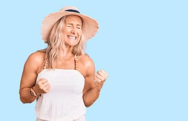 Middle age fit blonde woman wearing summer hat excited for success with arms raised and eyes closed celebrating victory smiling. winner concept.