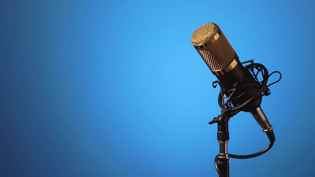 Micr&oacute;fono de mesa con cable montado sobre su base, haciendo giros y con cambios de iluminaci&oacute;n, con un fondo de color azul degradado.