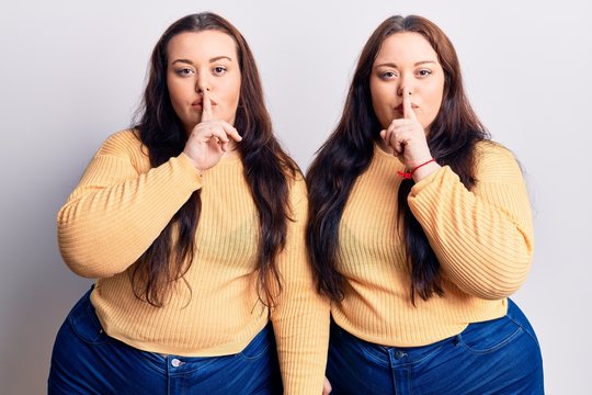 Young plus size twins wearing casual clothes asking to be quiet with finger on lips. silence and secret concept.