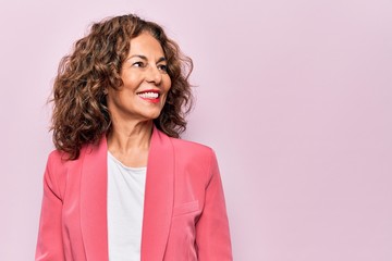 Middle age beautiful businesswoman wearing jacket standing over isolated pink background looking to...