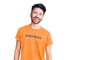 Young hispanic man wearing t shirt with happiness word message winking looking at the camera with sexy expression, cheerful and happy face.