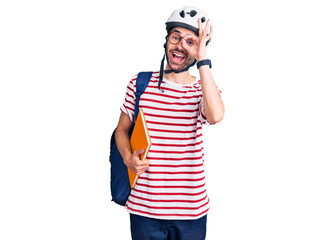 Young hispanic man wearing student backpack and bike helmet holding binder smiling happy doing ok sign with hand on eye looking through fingers