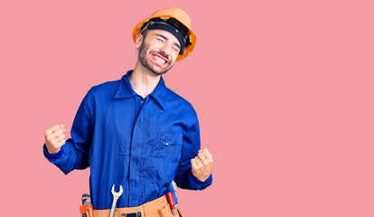 Young hispanic man wearing worker uniform very happy and excited doing winner gesture with arms raised, smiling and screaming for success. celebration concept.