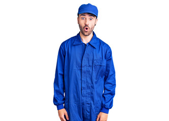 Young hispanic man wearing painter uniform scared and amazed with open mouth for surprise, disbelief face