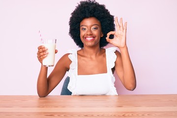 Young african american woman holding glass of milk doing ok sign with fingers, smiling friendly gesturing excellent symbol
